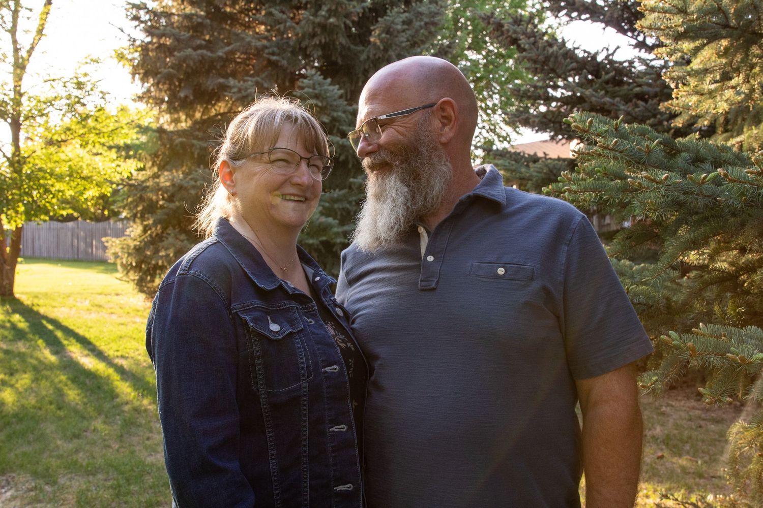 a couple stands together with trees in the background.