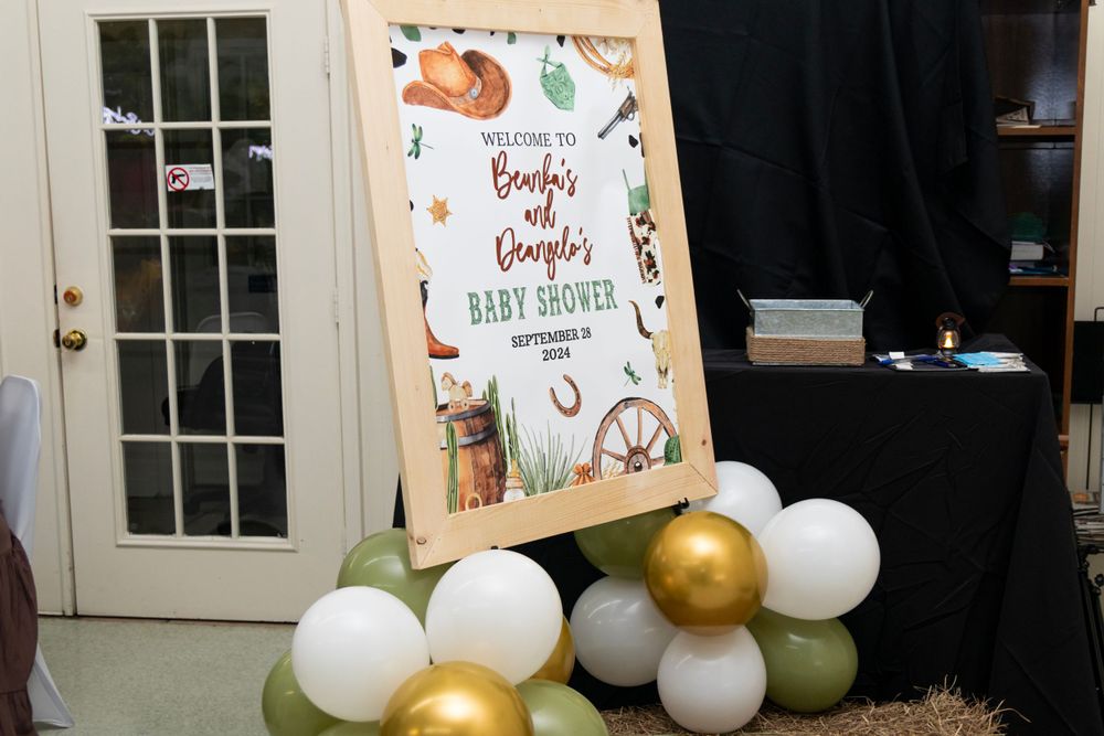 A party decoration setup with a welcome sign and an arch made of gold, white and olive green balloons.