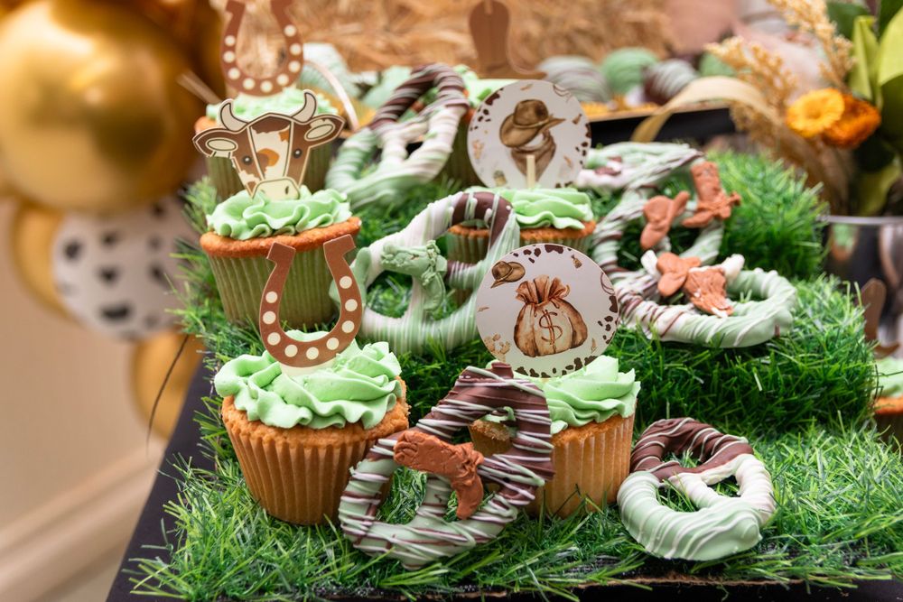 Safari themed cupcakes decorated with animal toppers on artificial grass display.