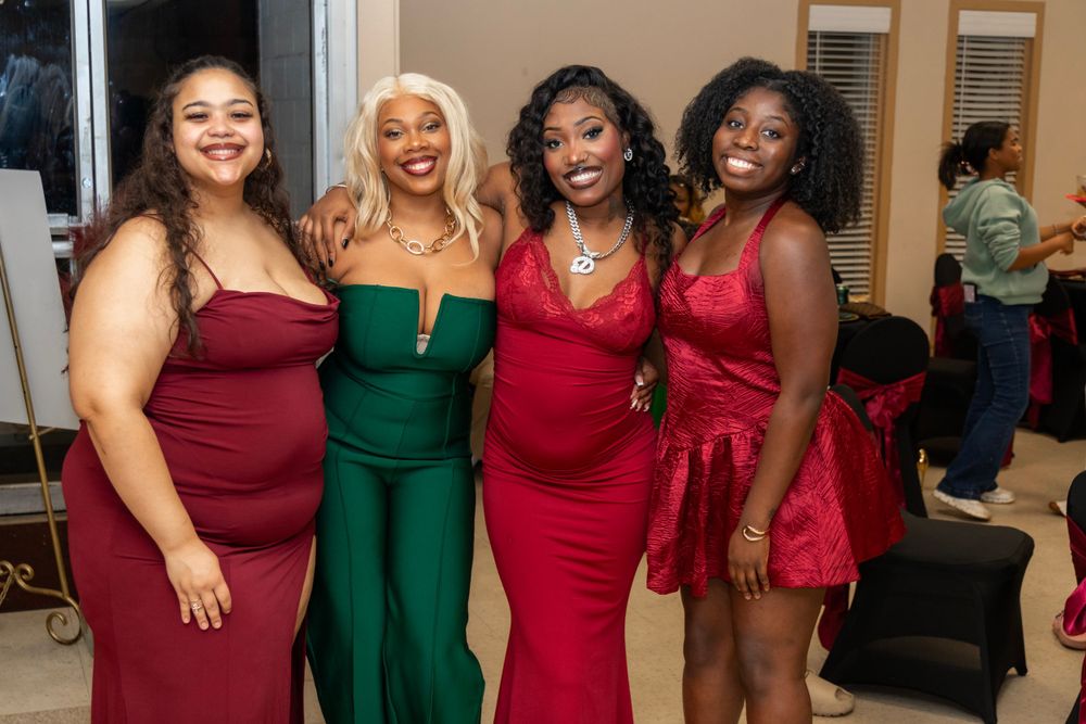 A group of friends pose together at a formal event wearing elegant dresses in red and emerald green colors.