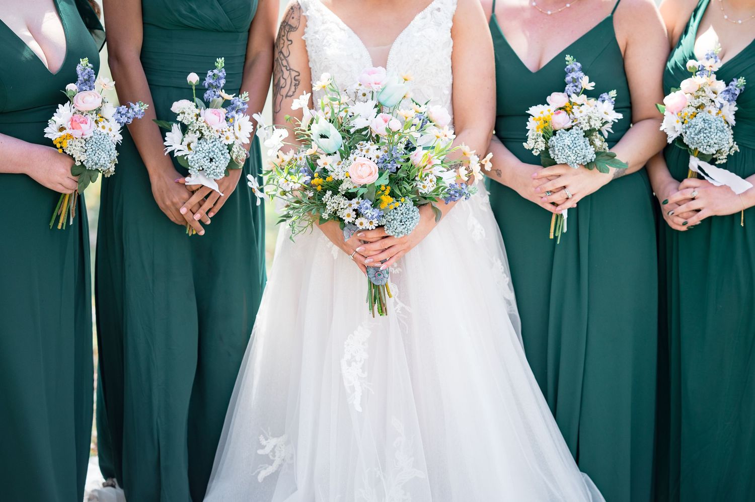 Row of bridesmaids in emerald green dresses holding matching blue and white bouquets.