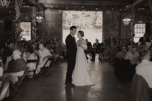 Bride and groom share their first dance in a rustic barn wedding venue surrounded by seated guests.