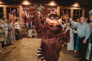 A mascot costume character dancing at a festive indoor wedding reception with string lights and guests celebrating.