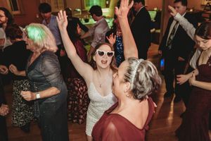 Guests dancing joyfully at a wedding reception, with a woman in sunglasses raising her arms in celebration.