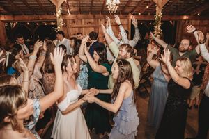 Wedding guests dancing with hands raised at a rustic barn reception celebration.