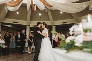 Bride and groom share first dance kiss at elegant wedding reception with guests watching in decorated venue.