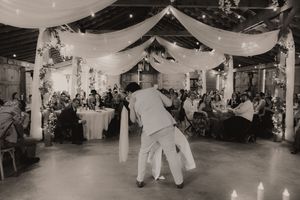 Black and white photo of couple sharing first dance at elegant wedding reception with draped ceiling lights.