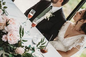 Bride and groom sharing a romantic moment at wedding reception table with champagne glasses and blush pink roses.