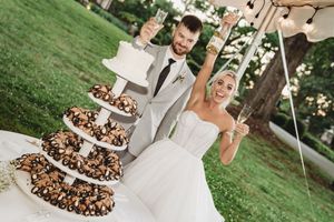 Bride and groom celebrate at outdoor wedding with tiered chocolate dessert tower and small white cake.