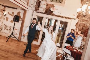 Bride and groom share first dance at rustic wedding reception venue with exposed brick walls and wood floors.