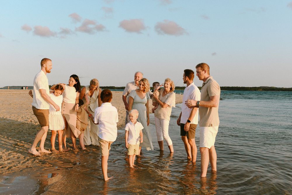 Large group enjoying beach celebration in casual white attire at sunset.