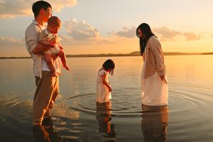 A family stands together in shallow water during a beautiful golden sunset at the beach.