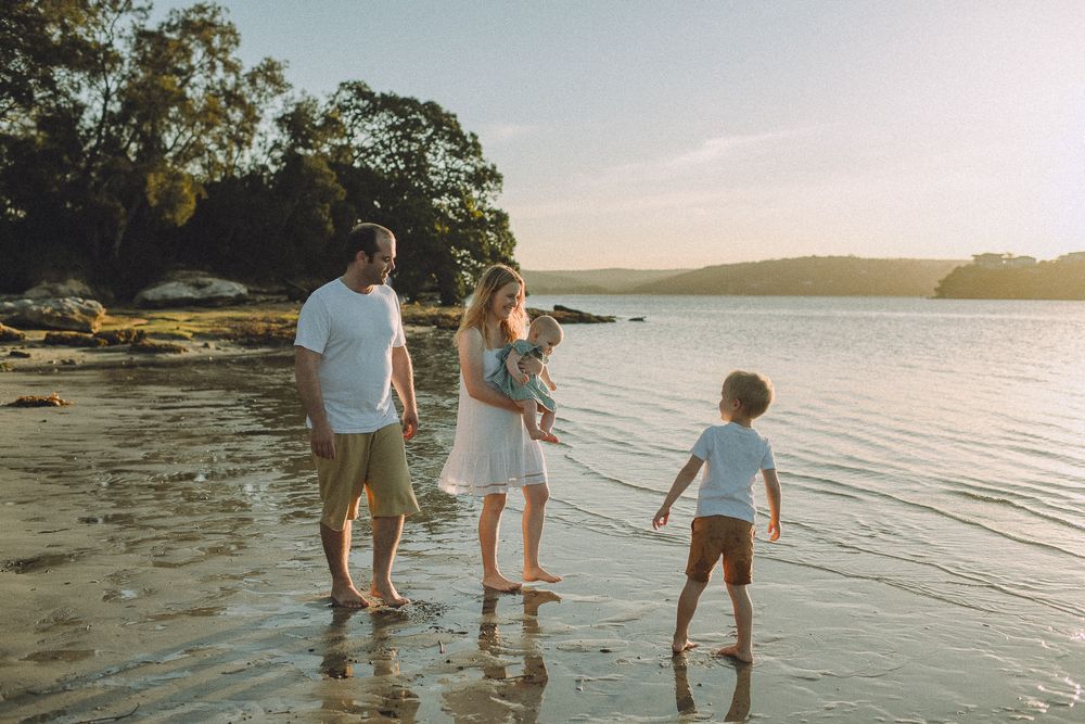 Family walks along shoreline at sunset enjoying peaceful beach moment together.
