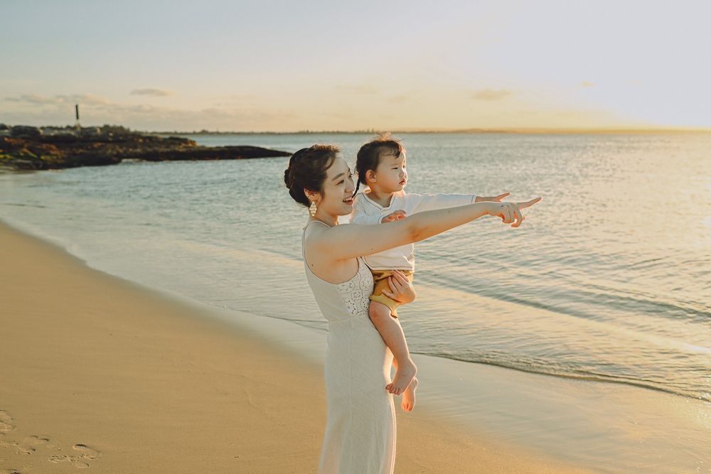 Two people share a tender moment while pointing at the horizon on a beautiful beach at sunset.