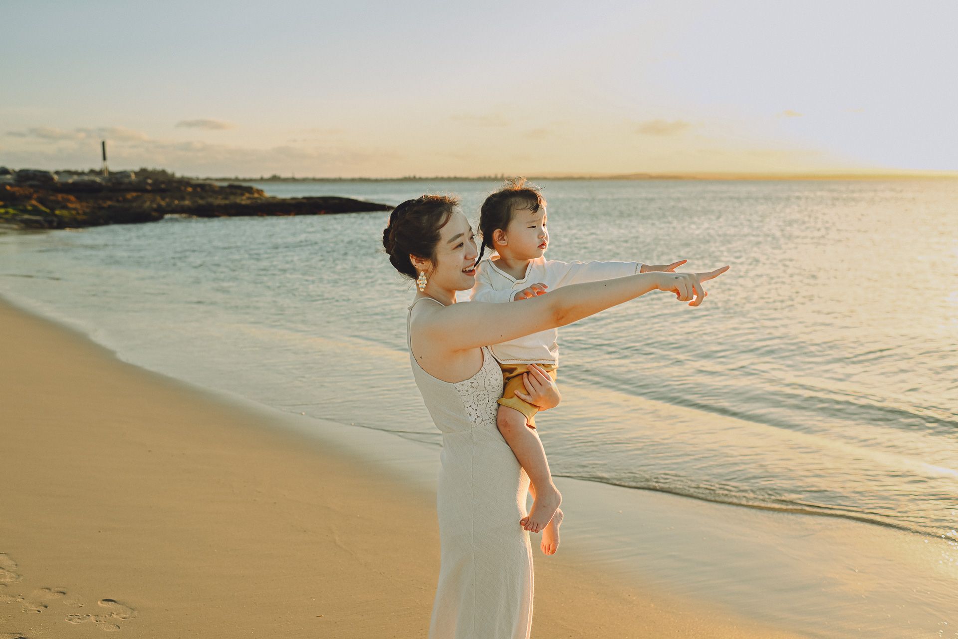 Two people share a tender moment while pointing at the horizon on a beautiful beach at sunset.