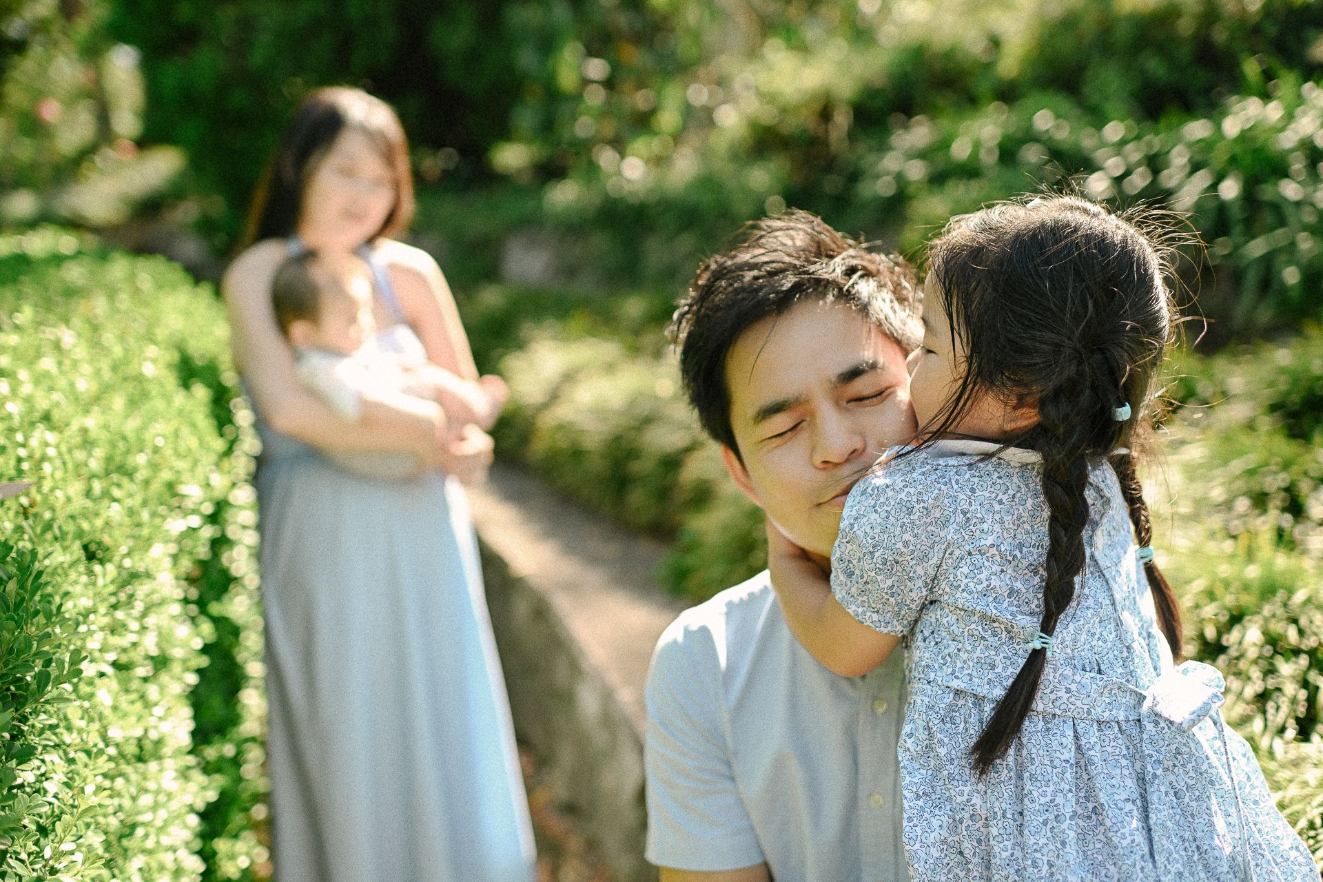 A tender family moment captured in a lush garden setting. A father kneels down, receiving a loving hug from his daughter