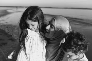A black and white photograph of a mother wearing a hijab, lovingly holding her two young daughters at Ramsgate Beach.