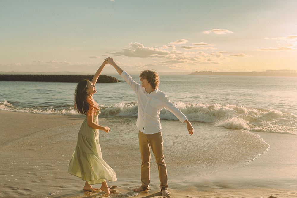 Couple dancing together on beach at sunset with ocean waves in background.