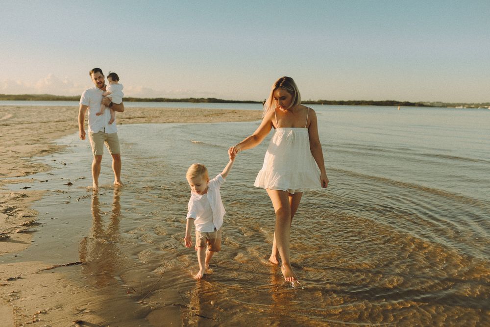 A family walking barefoot along Ramsgate beach at sunset, with a mother holding her young son's hand