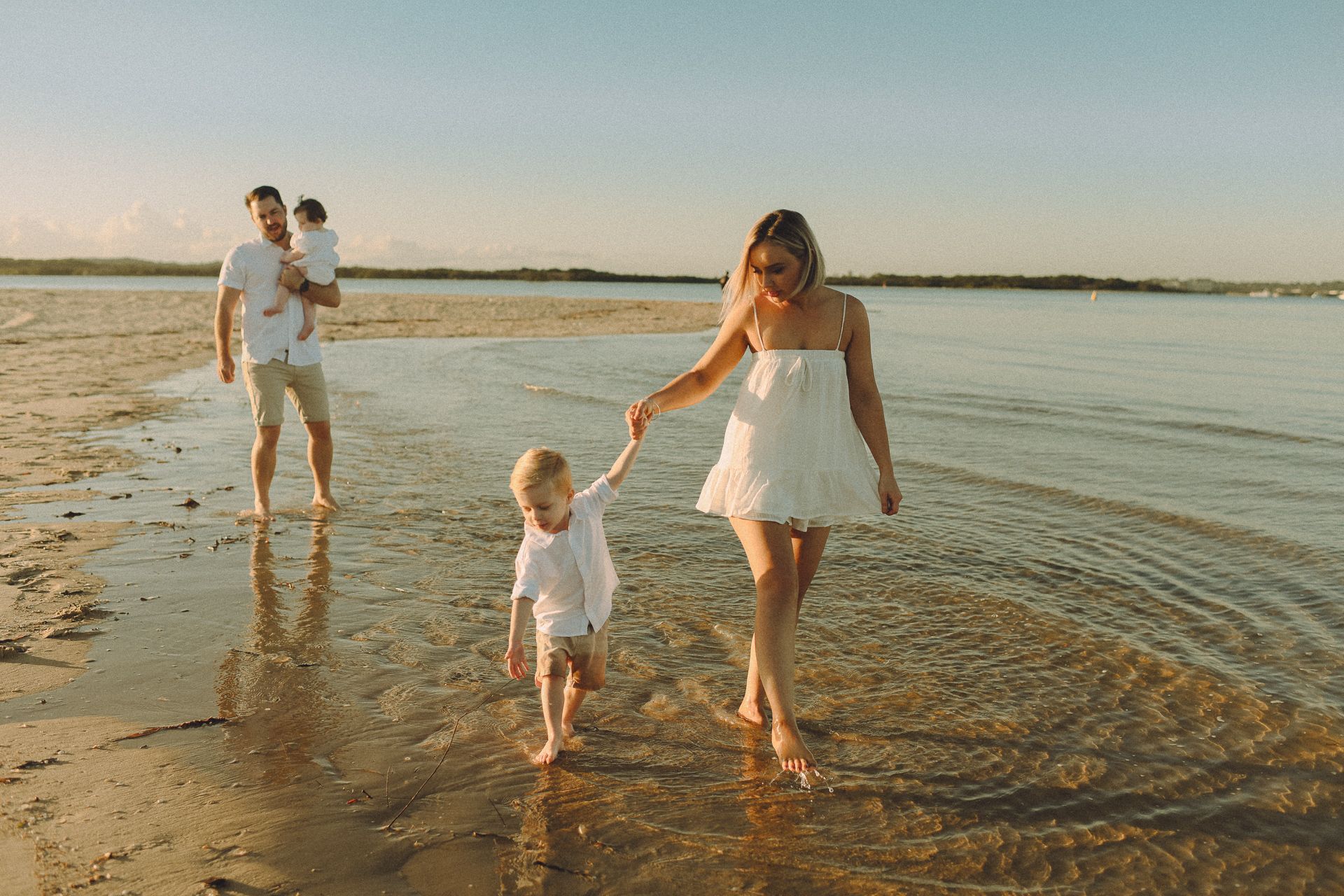 A family walking barefoot along Ramsgate beach at sunset, with a mother holding her young son's hand