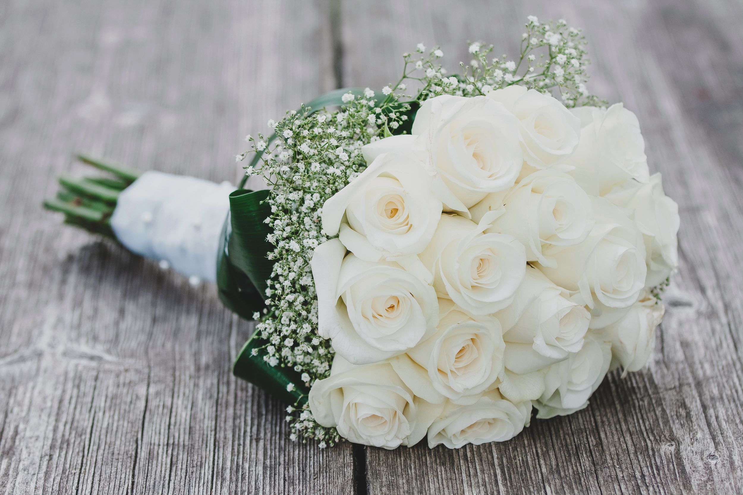 A classic white rose bridal bouquet with baby's breath lies on a rustic wooden surface.