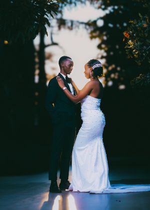A romantic wedding couple in formal attire embrace during a sunset outdoor photo session.