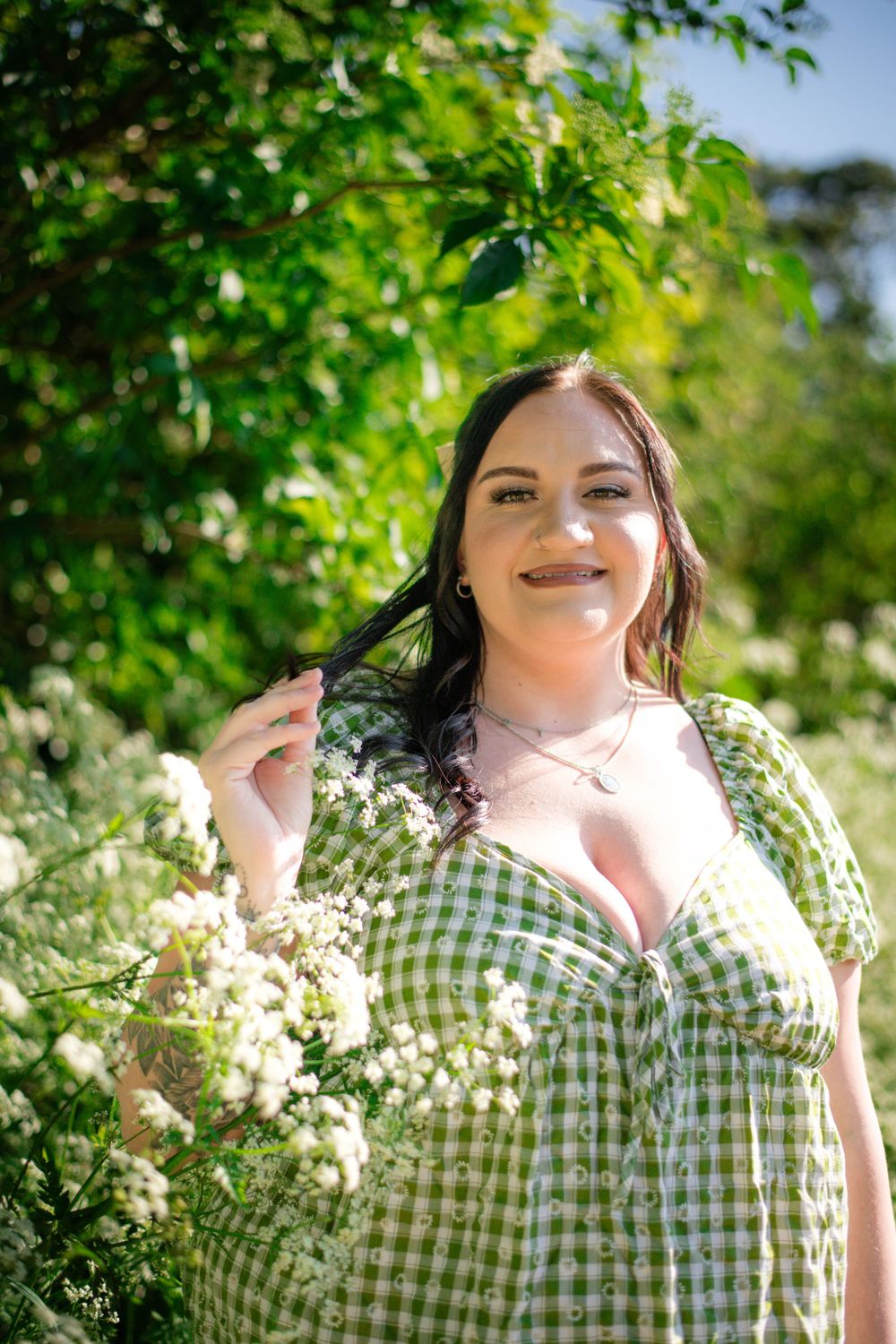 Woman in checkered dress smiling in garden with white flowers and green foliage.