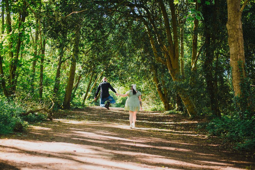 Two people walking hand in hand down tree-lined path on sunny day.