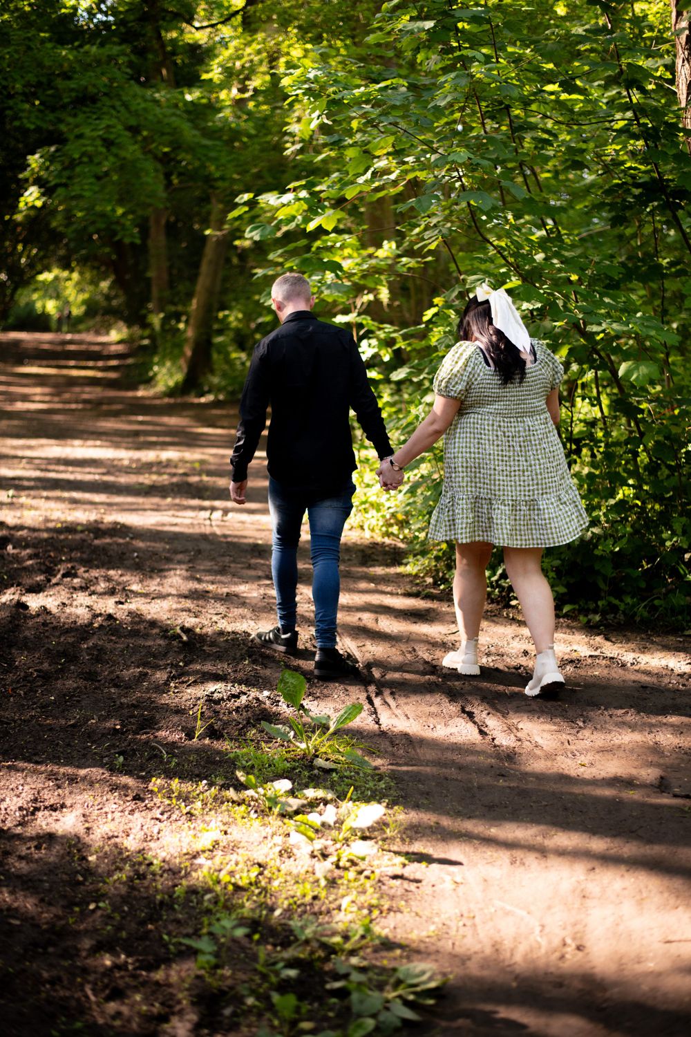 Two people hold hands while walking down a wooded trail in summer.