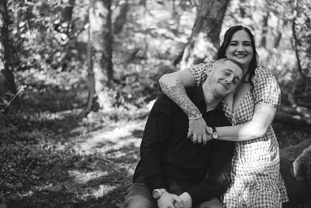 A black and white photo captures a tender embrace in a forest setting.