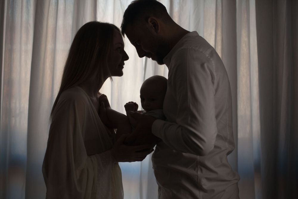 coppia con figlio baby in controluce, sessione famiglia, sessione fotografica baby a domicilio a Peschiera Borromeo, mamma e papà abbraccio