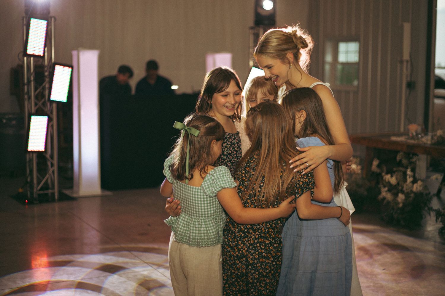 An emotional group hug moment during a wedding reception on a dimly lit dance floor.