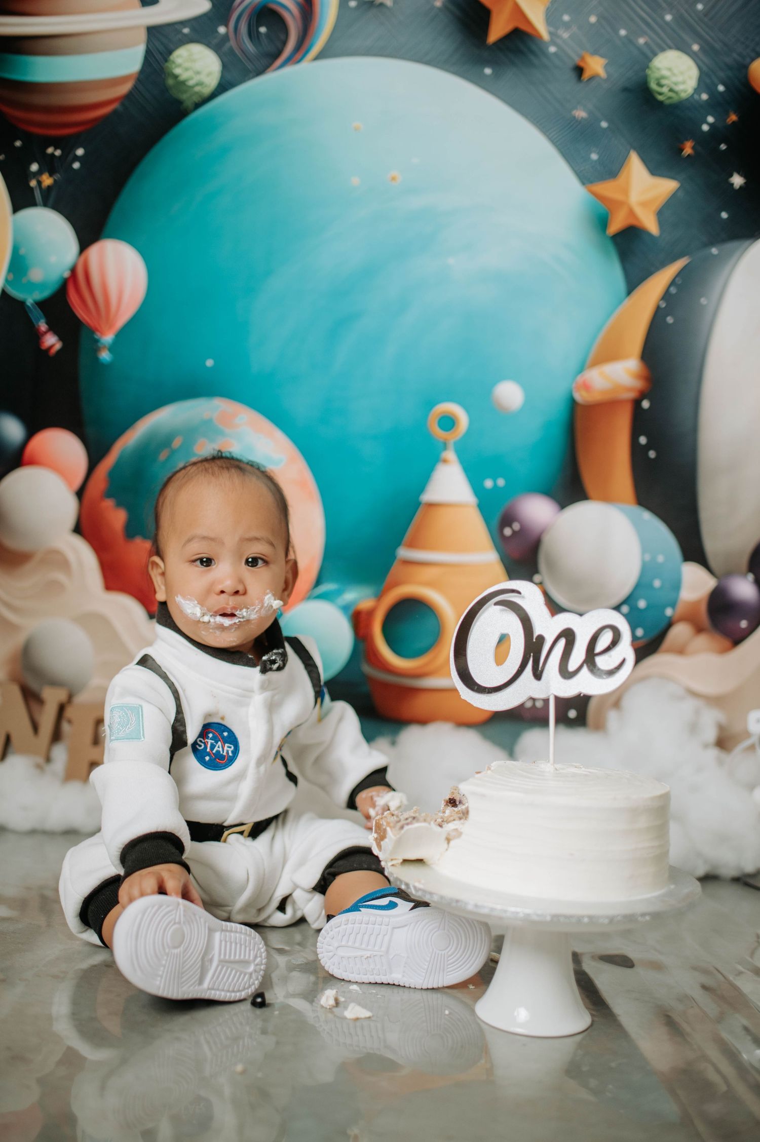 First birthday space-themed celebration with cake and celestial decorations against turquoise backdrop.