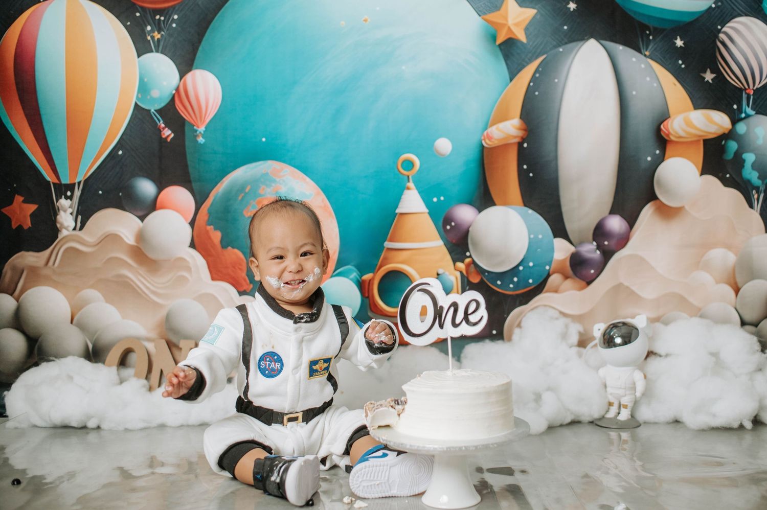 First birthday photoshoot featuring space theme with rockets, stars, and cloud decorations.