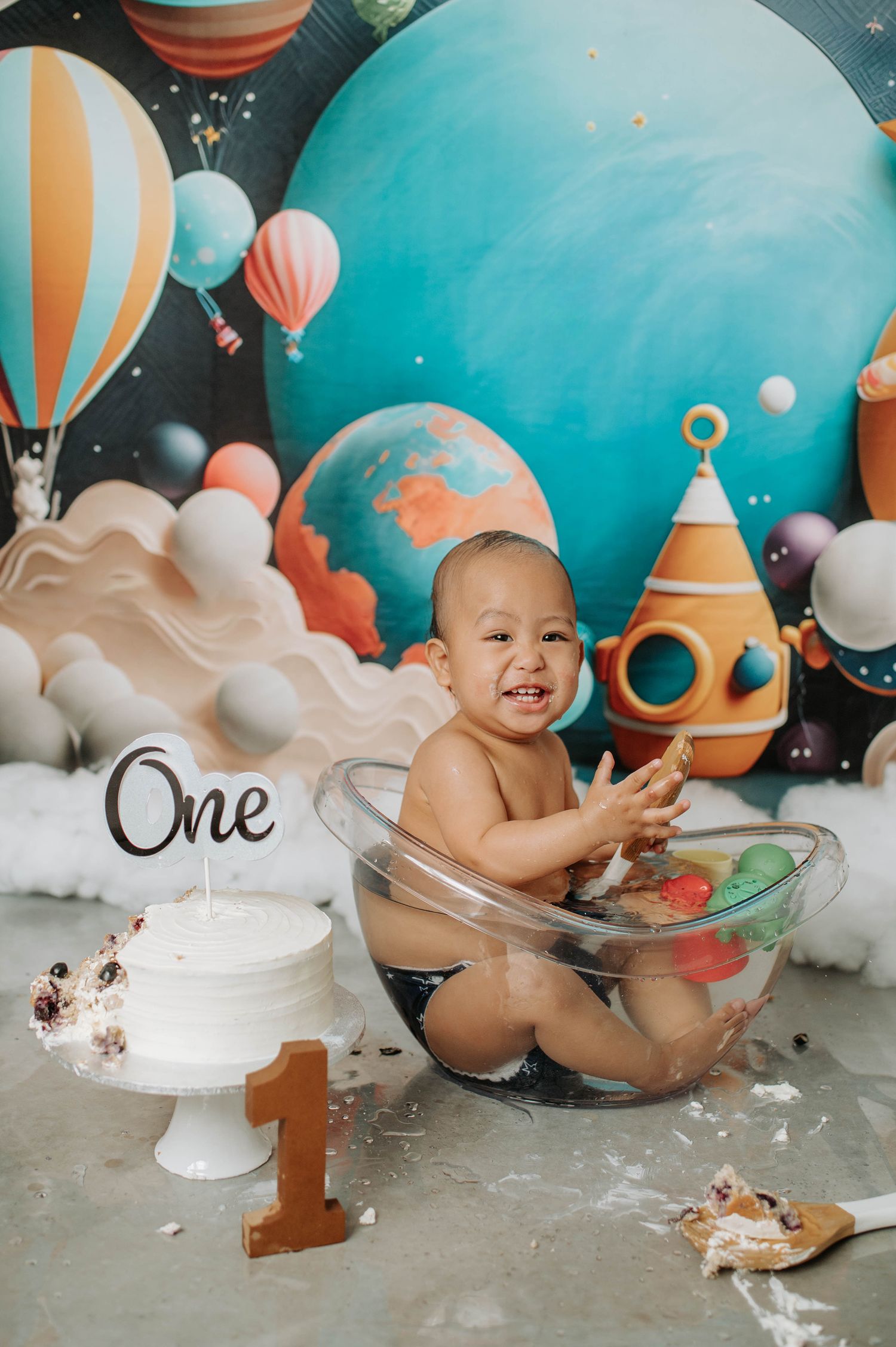 Space-themed cake smash session with clear bowl, white cake, and cosmic backdrop.