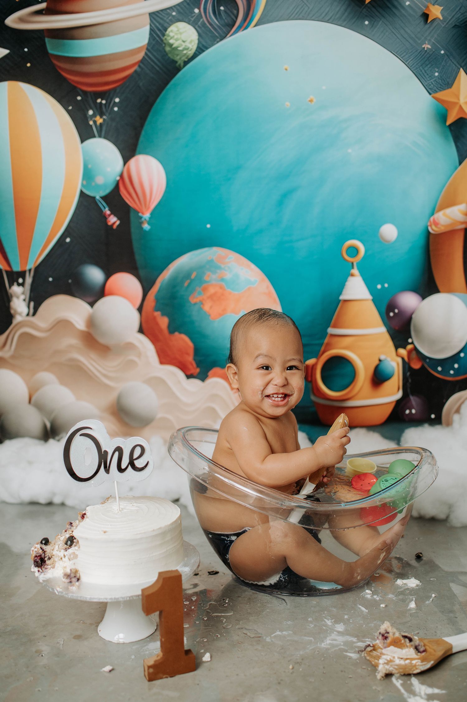 Cosmic cake smash photography setup with clear bowl and space-themed background decorations.