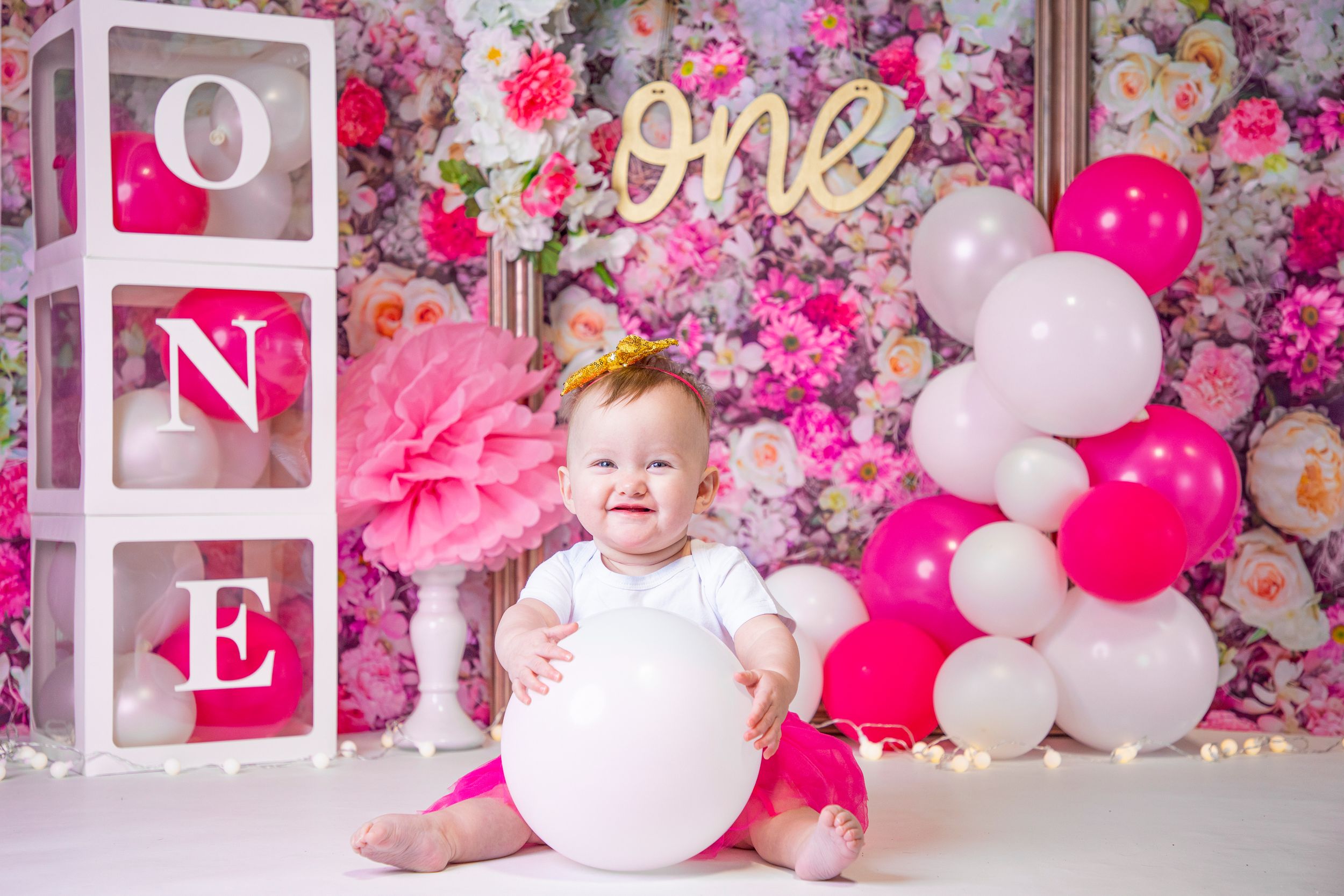 Pink floral backdrop with white letter blocks and balloons for birthday celebration.