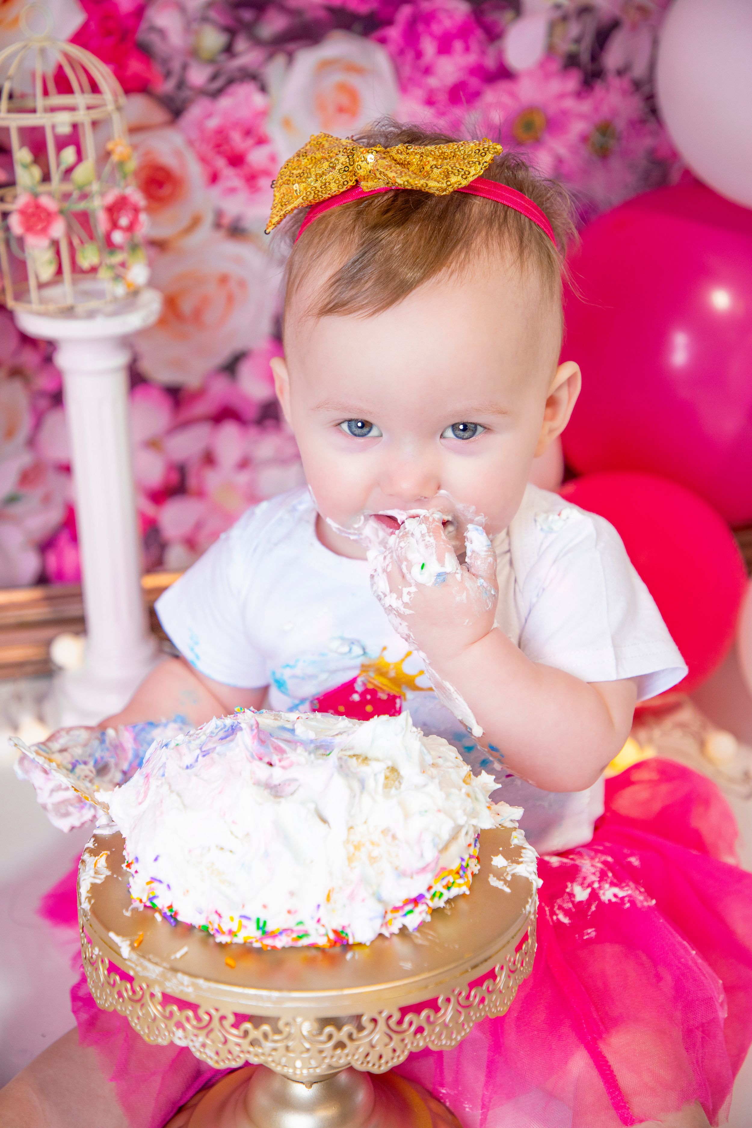 Birthday cake smash session with gold stand and pink floral backdrop.