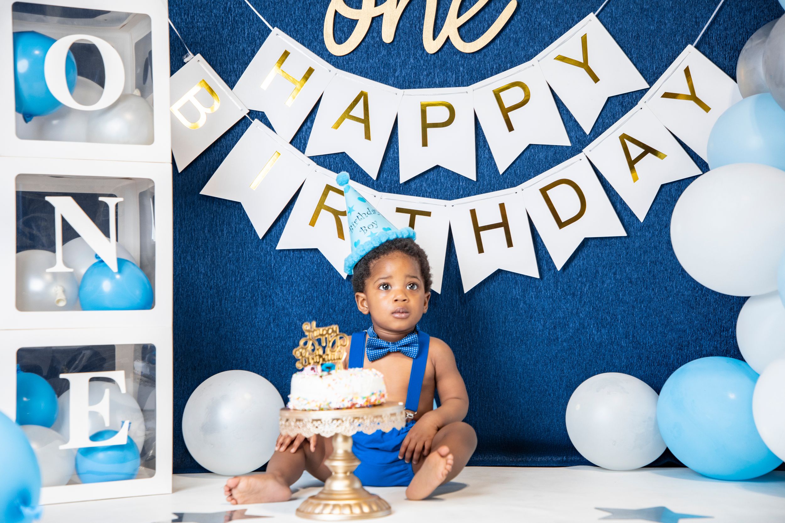 Blue and white balloon arch with happy birthday banner against navy backdrop.