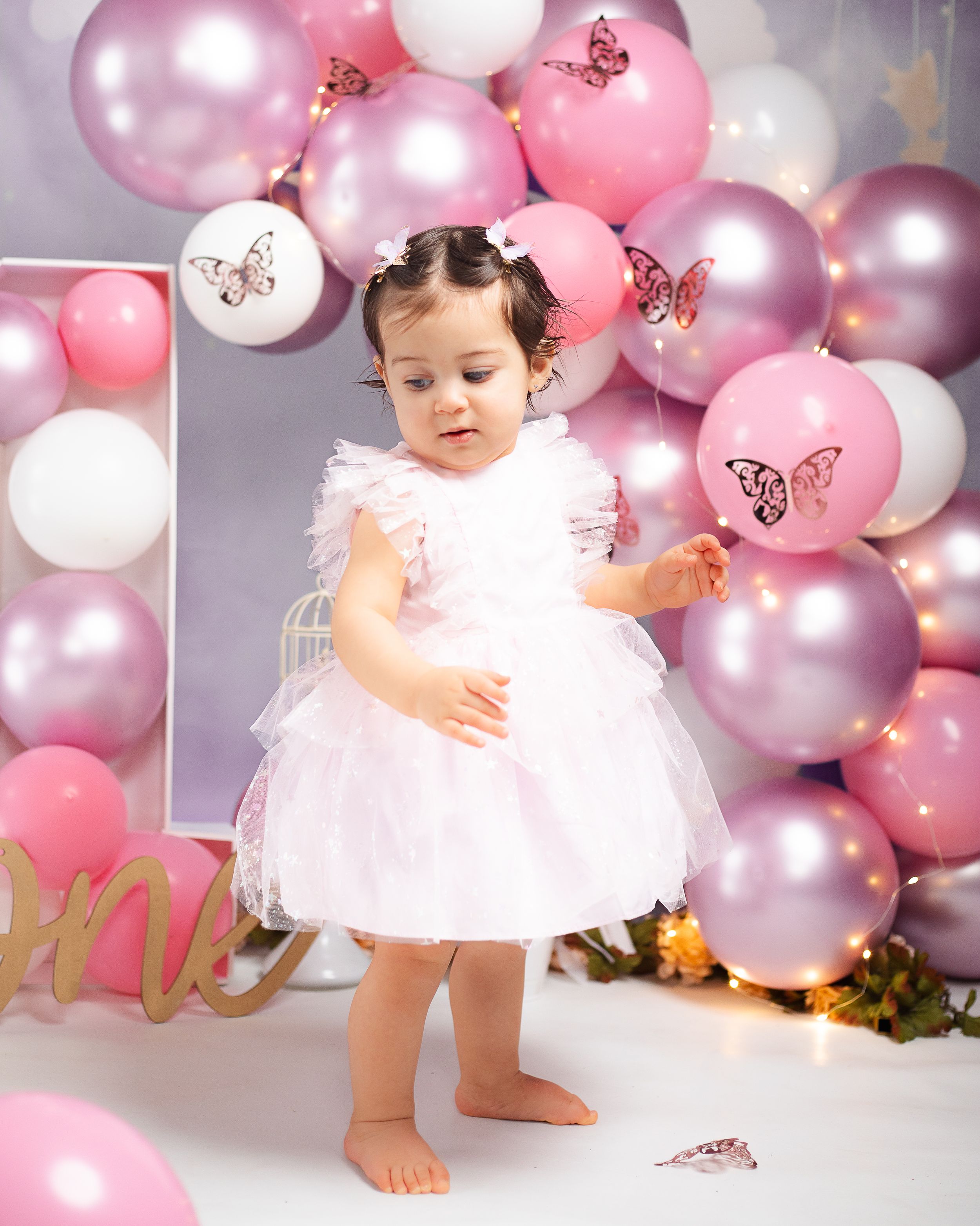 Pink and white balloon arch creates dreamy backdrop for first birthday cake smash photoshoot.