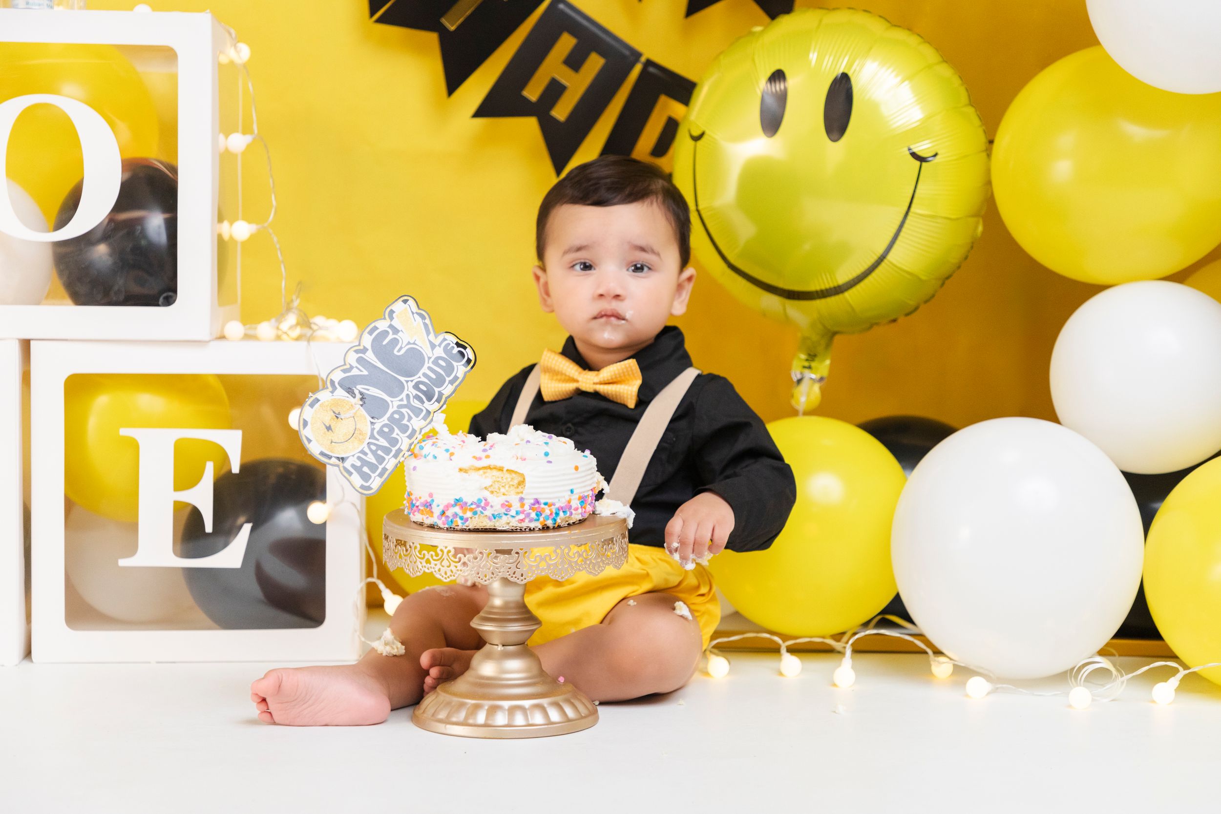 Yellow balloon backdrop with smiley faces creates cheerful birthday setting.