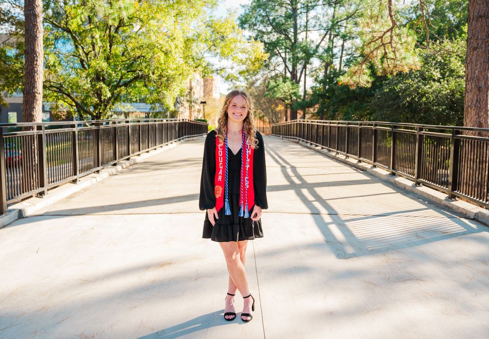 Columbus State University Graduate wearing red Cougar Athletics graduation stoles with a black v-neck dress poses outdoors.