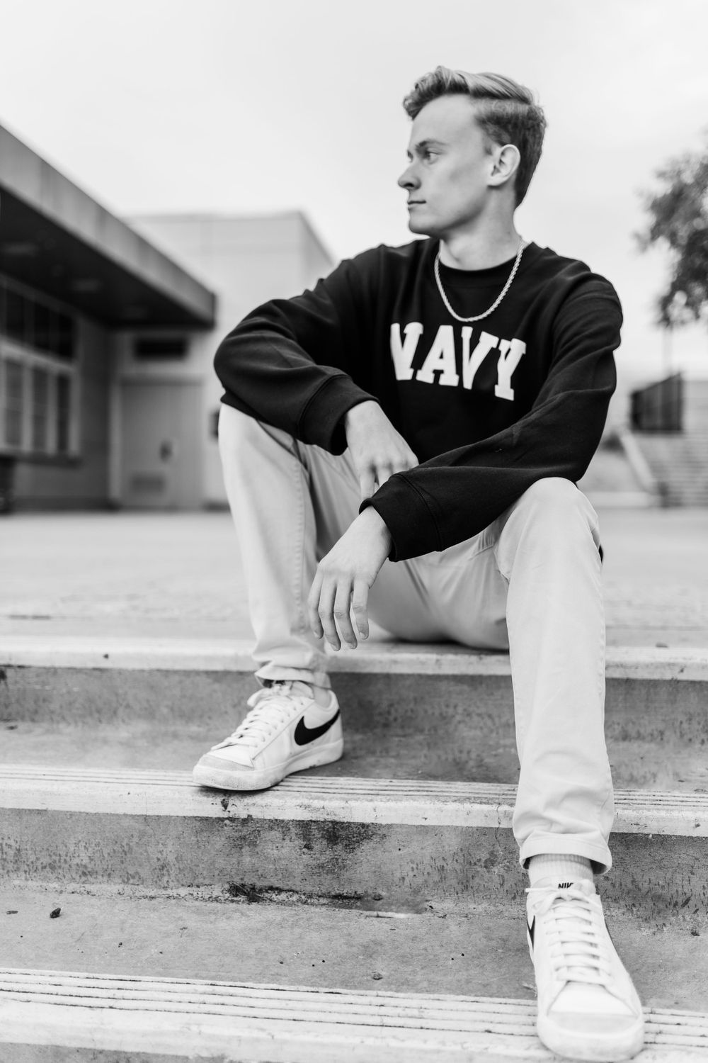 Black and white portrait of someone wearing a Navy sweatshirt and white sneakers sitting on concrete steps.