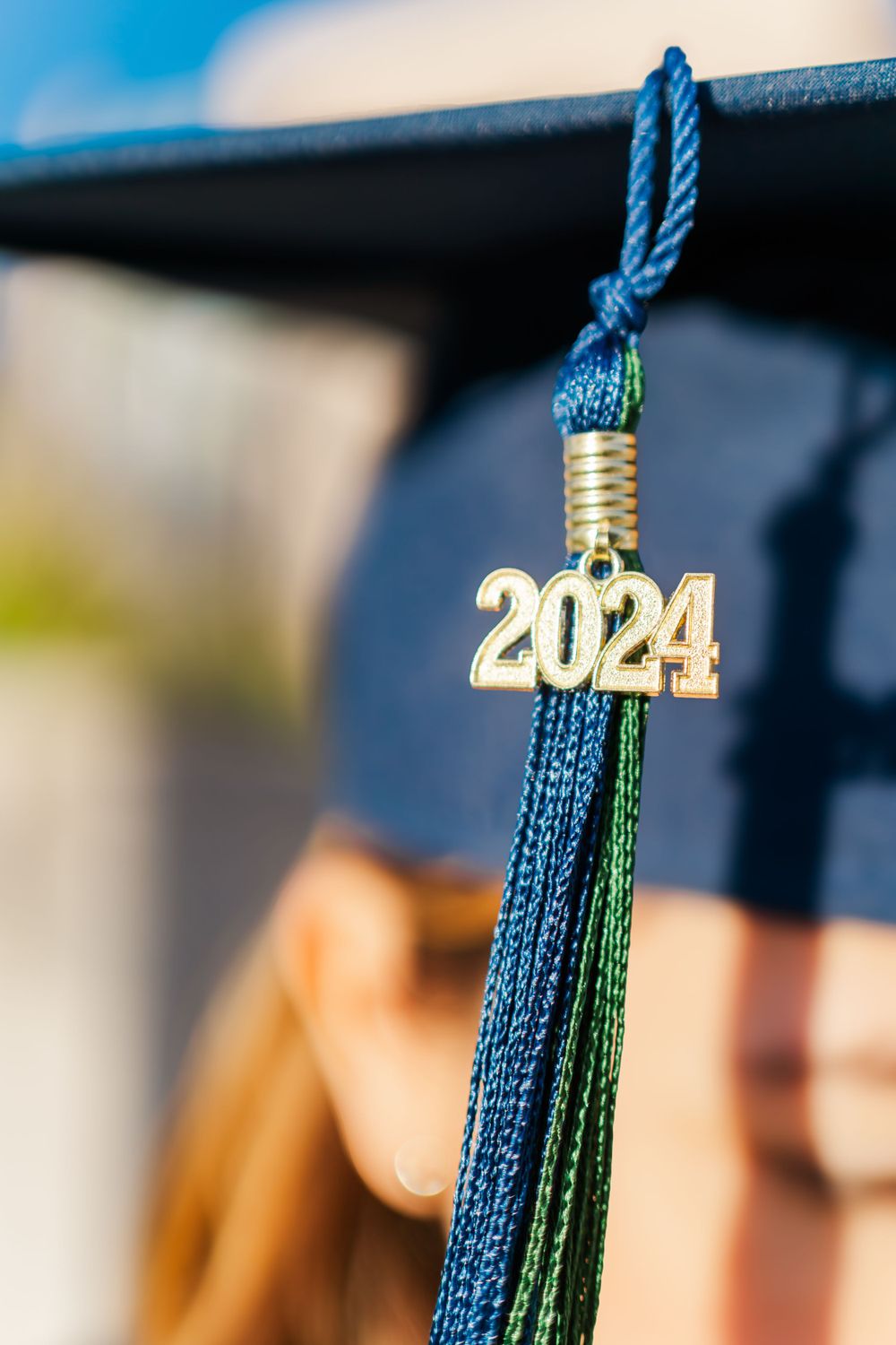 Close-up of a blue and green graduation tassel with gold 2024 charm hanging from a mortarboard cap.