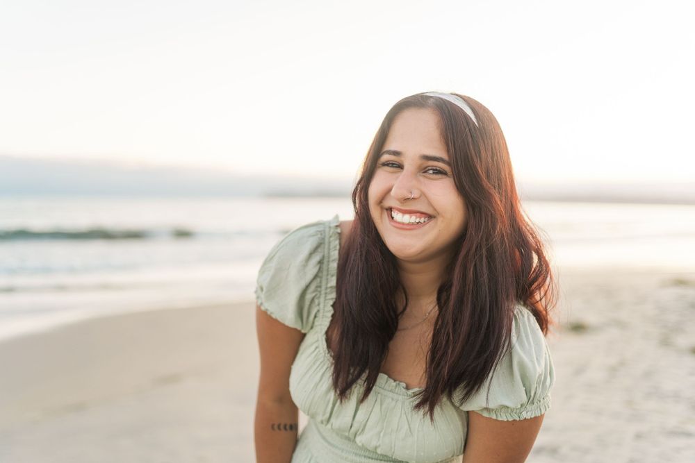 Woman in mint green dress smiling at the beach during golden hour sunset.