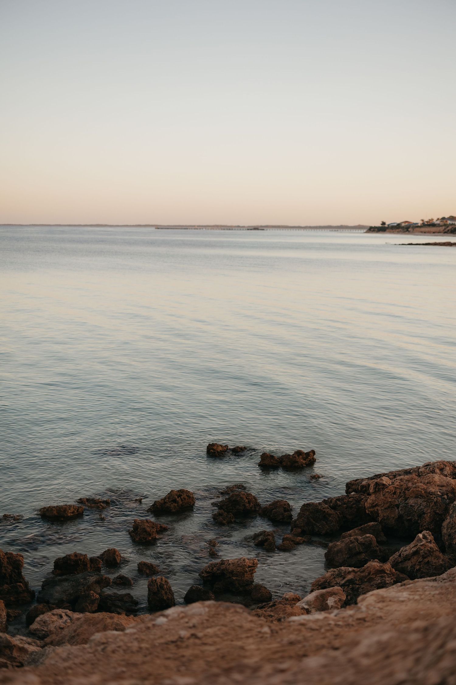 Calm ocean waters meet rocky coastline during golden hour.