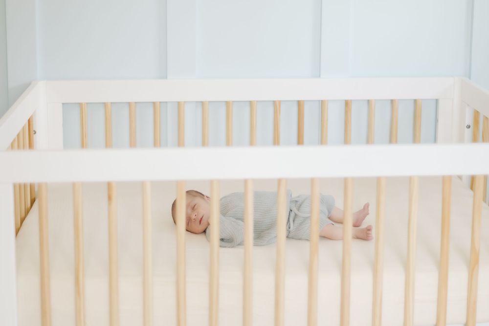 Sleeping infant rests peacefully in wooden crib with natural light streaming in.
