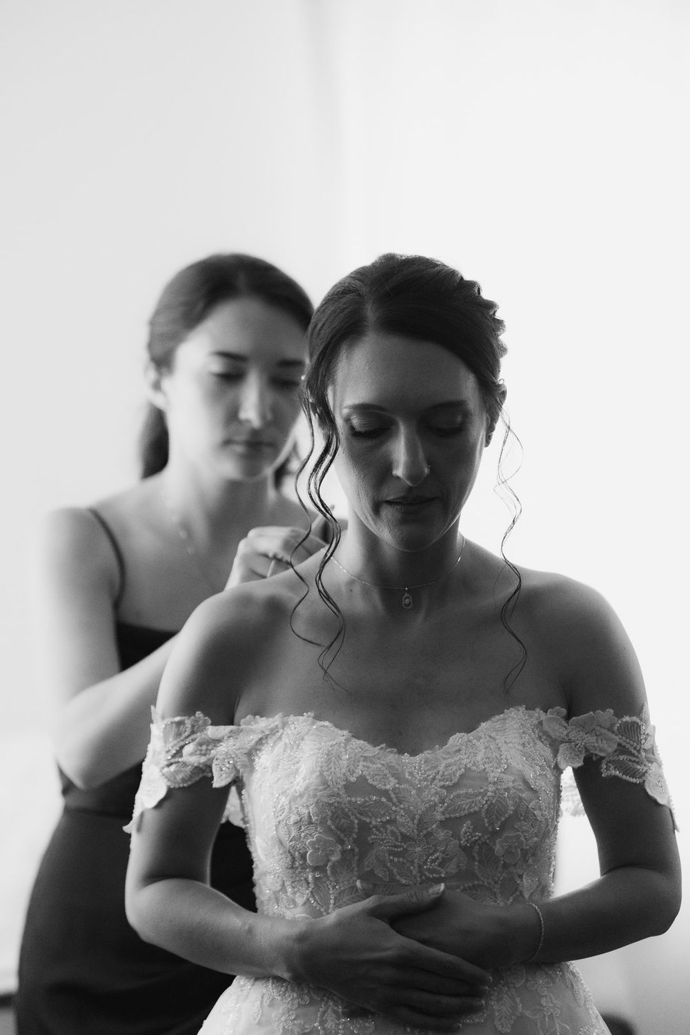 Bride getting ready as bridesmaid buttons lace gown, captured by Cleveland wedding photographer.