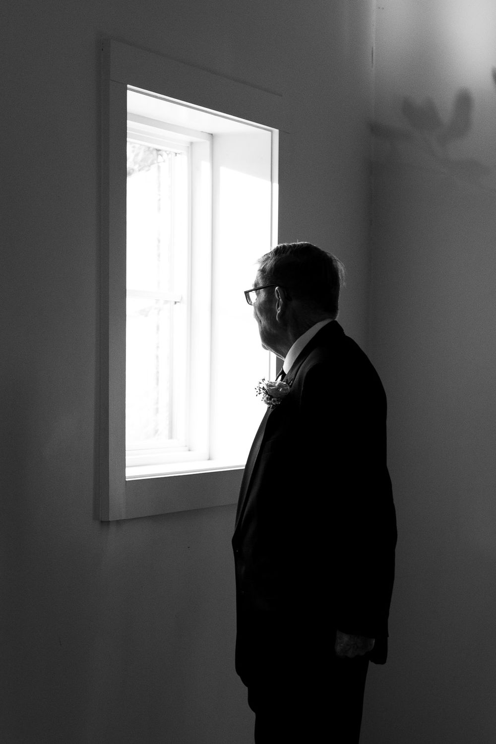Black and white edit of the father of the bride joyfully waiting by a window, captured by Cleveland wedding photographer.