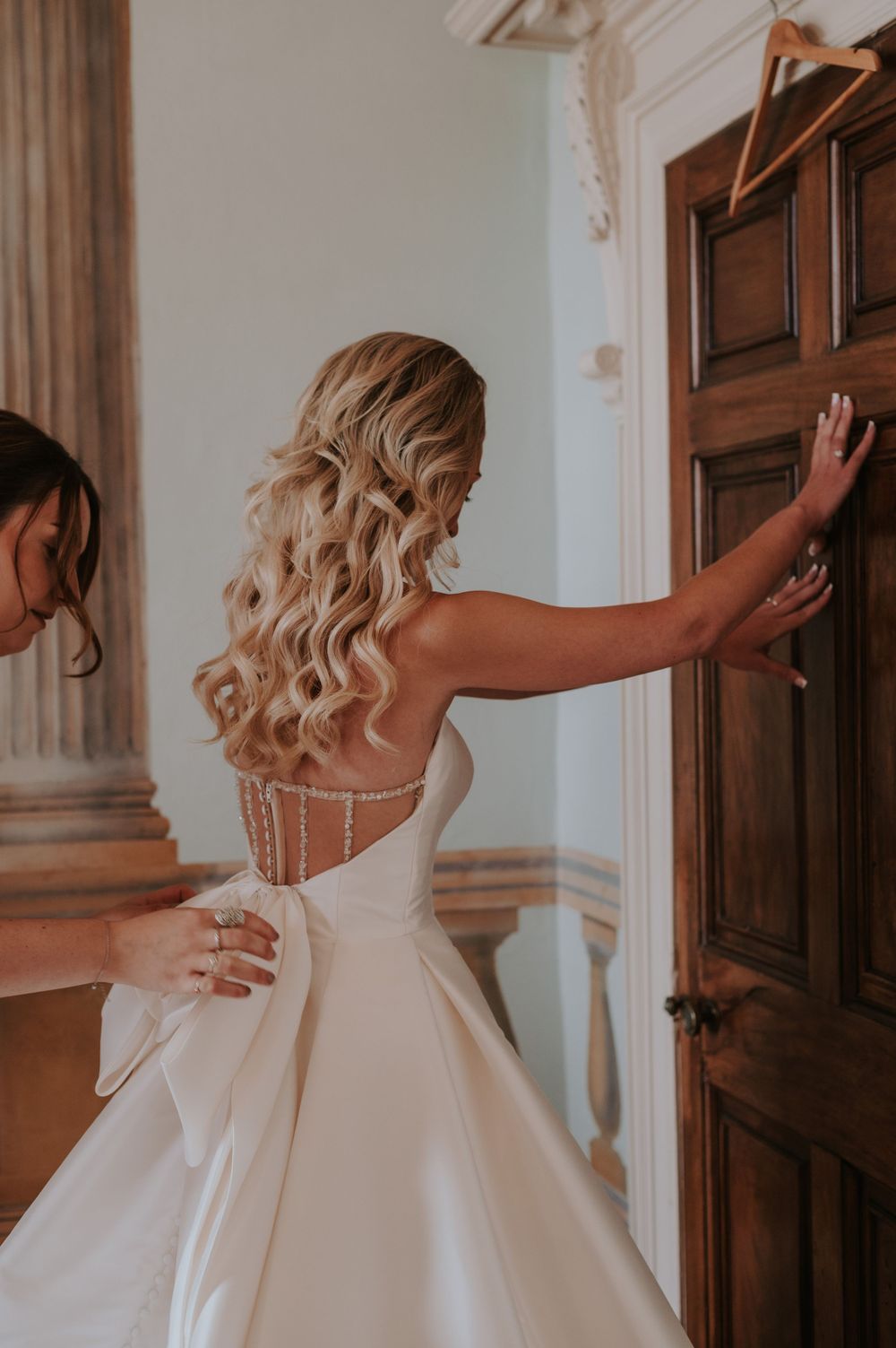 Elegant white wedding dress with corset back detail and flowing skirt shown from behind in ornate interior doorway.